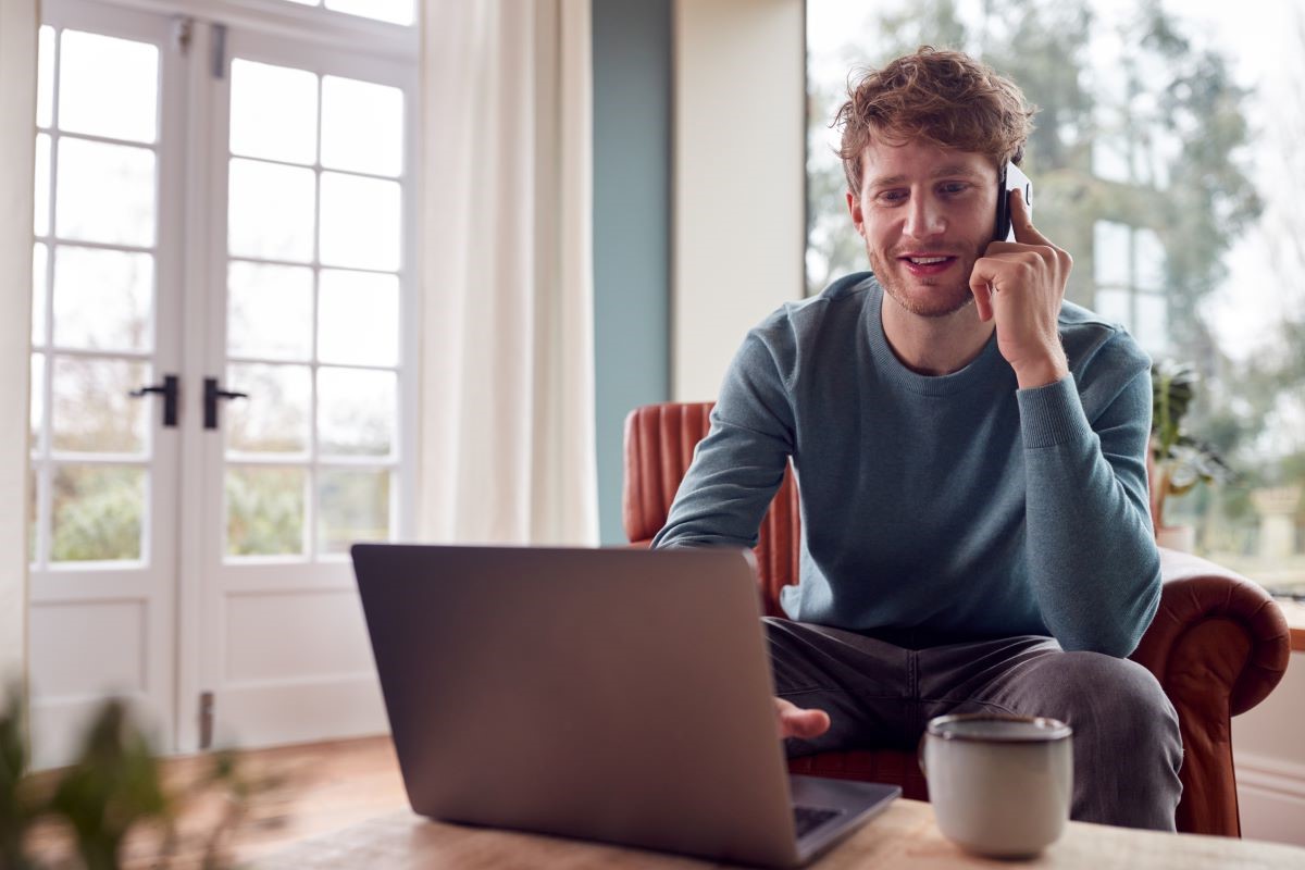 Man working from home with laptop and talking on mobile phone